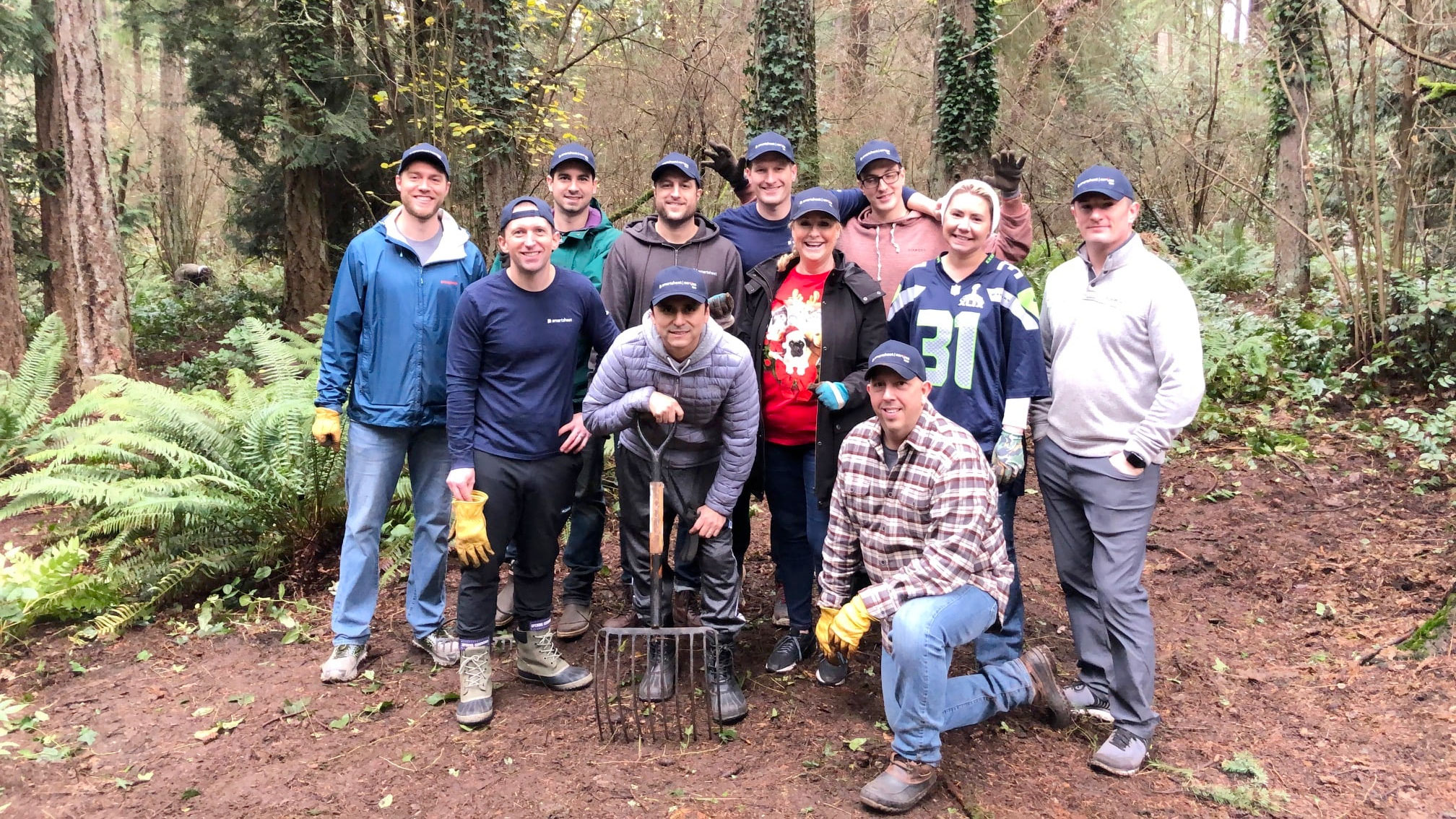 Smartsheet employees pose for a group photos amidst ferns and a wooded forest area.